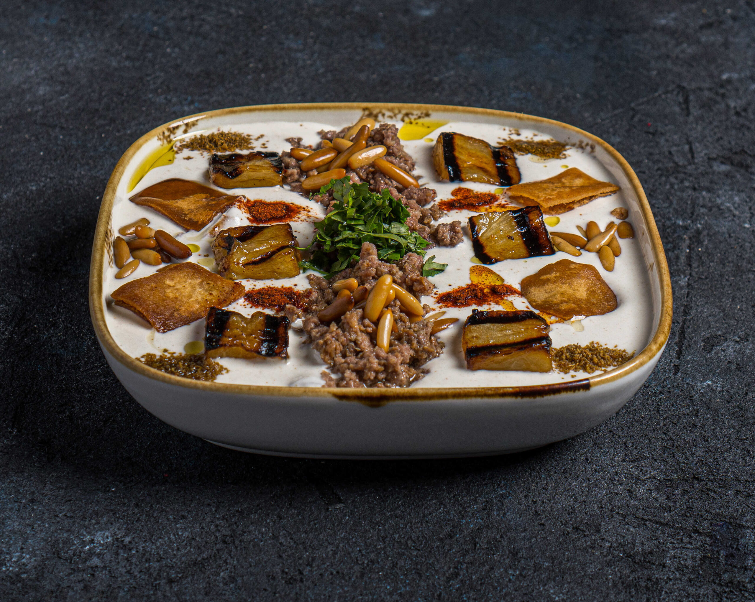 فتة باذنجان | Fatteh Eggplant قطع الباذنجان المقلي مع صوص الطحينة واللحم والصنوبر | Sliced fried eggplant with tahina sauce, meat and pinenut فتة باذنجان